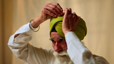 Fotografía-De-Estudio-De-Un-Hombre-Sikh-Mayor-Con-Barba-Que-Se-Coloca-Una-Aguja-De-Salai-En-Un-Turbante-Contra-Un-Fondo-Liso,-Filmado-En-Tiempo-Real